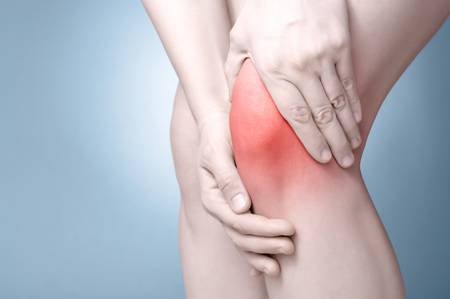 Eine Frau hält sich aufgrund von Knieschmerzen die Hände auf das Knie