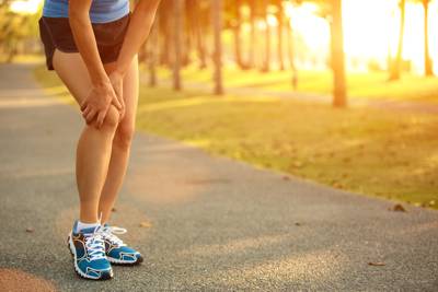 Eine Läuferin hält sich aufgrund Schmerzen beide Hände ans Kniegelenk