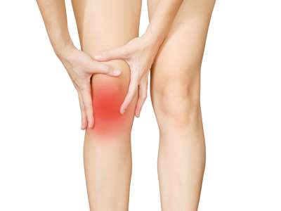 Eine Frau hält sich aufgrund von Knieschmerzen die Hände vorne auf das Knie